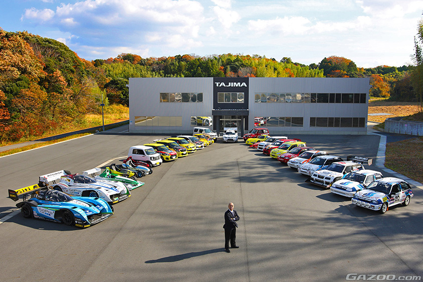 タジマモーターコーポレーションの袋井次世代モビリティー研究開発センターに並べられた歴代マシンたちと写真に収まるモンスター田嶋