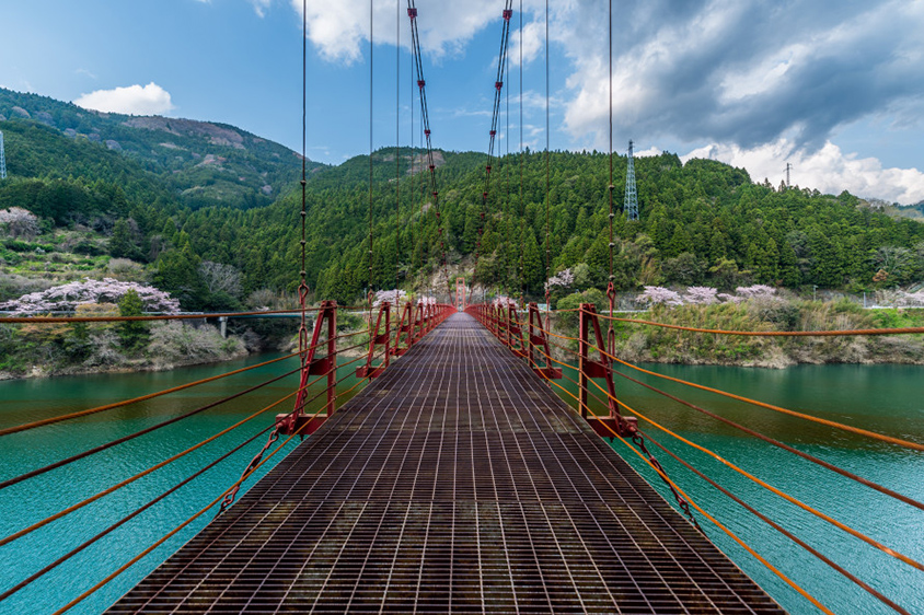 青い水面に赤い吊り橋が鮮やか。スリル満点だが、頑張って渡ってみよう。