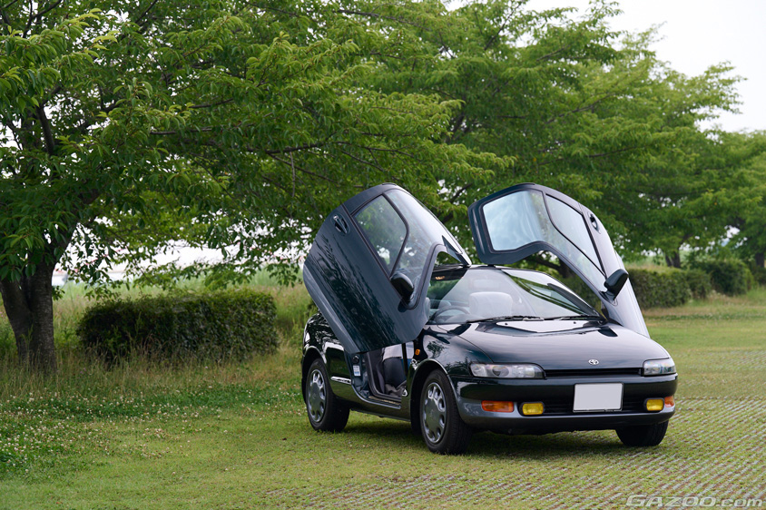 緑の木々をバックにバタフライドアを開いたトヨタ・アムラックスセラ