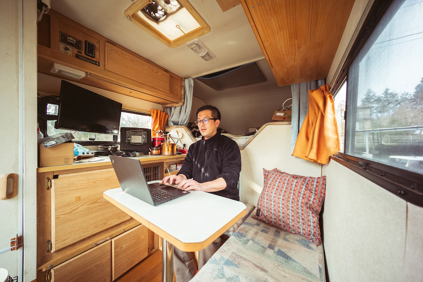 トヨタ・ハイラックスのピックアップキャビンの中で仕事をする宮本さん