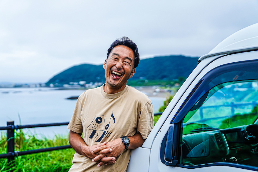 スズキ・エブリイにもたれ笑顔を見せる塚越さん