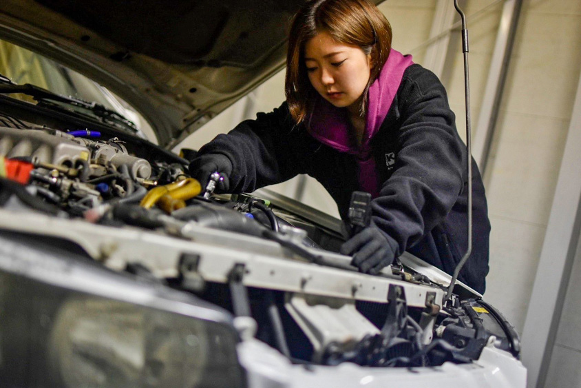 日産・R34スカイラインのエンジンルームをメンテナンスするMayuさん