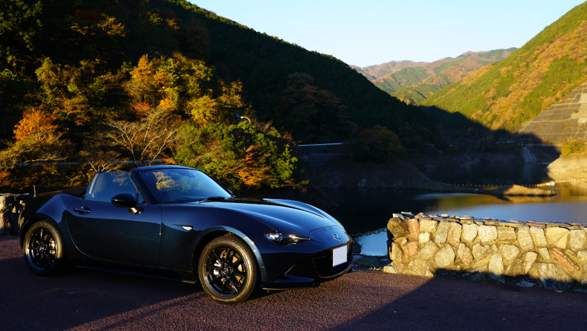 朝日に照らされるマツダ・NDロードスターと紅葉