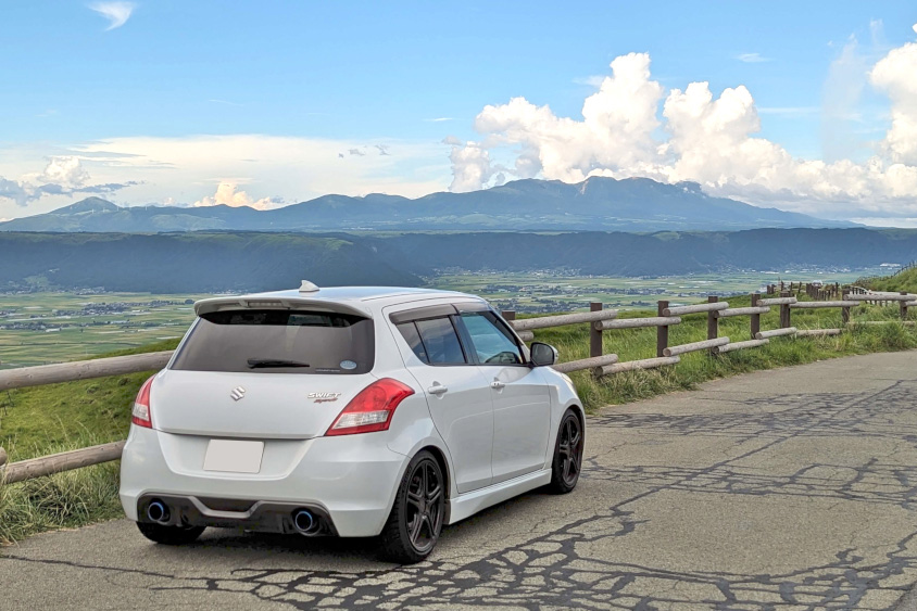 スズキ・スイフトスポーツのリヤと阿蘇の山並み