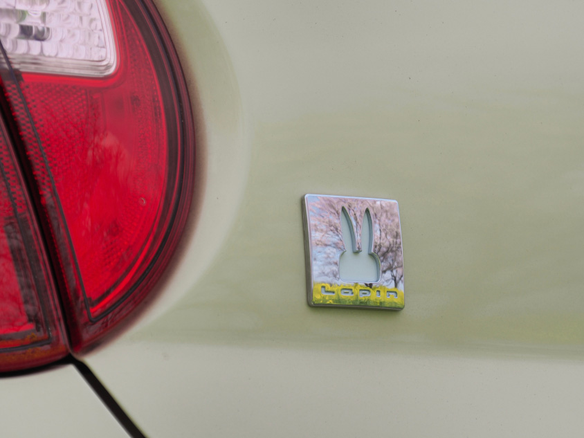 花が映り込んだスズキ・アルト ラパンのリヤのウサギのエンブレム