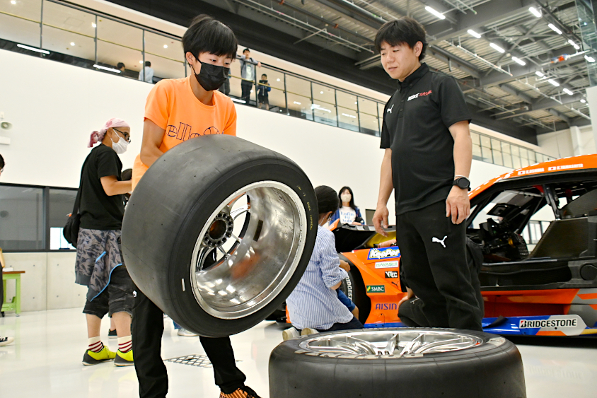 SUPER GTのタイヤとホイールを持ち上げるROOKIE Racingキッズガレージツアー参加者