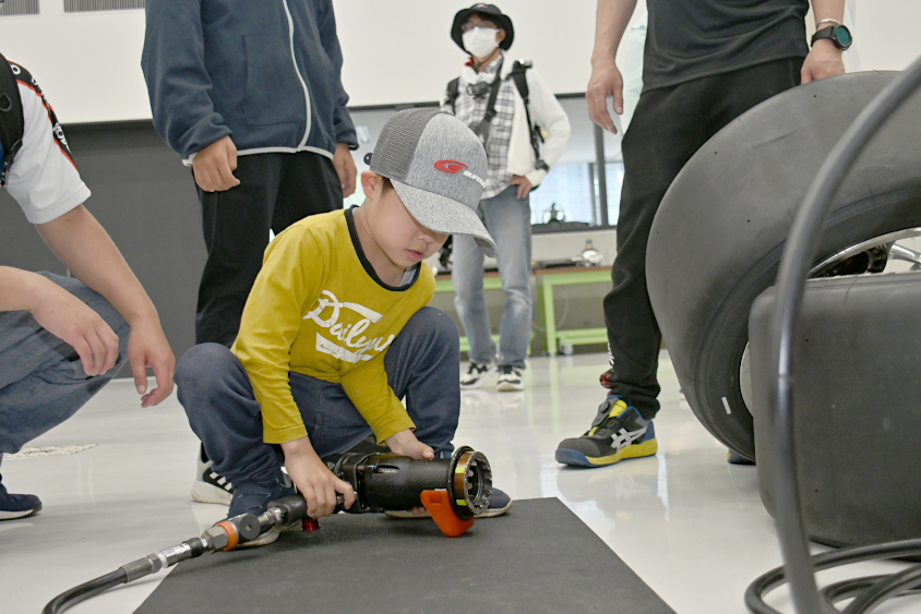 SUPER GTのインパクトレンチを持ち上げるROOKIE Racingキッズガレージツアー参加者