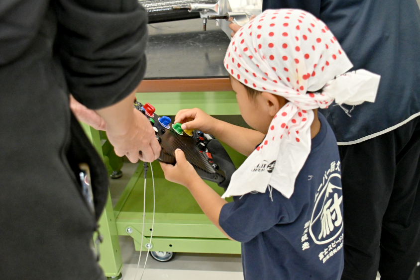 SUPER GTのステアリングを触るROOKIE Racingキッズガレージツアー参加者