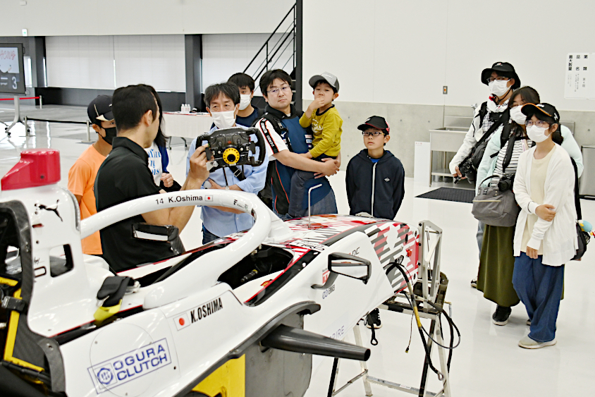 スーパーフォーミュラマシンの説明を聞くROOKIE Racingキッズガレージツアーの参加者