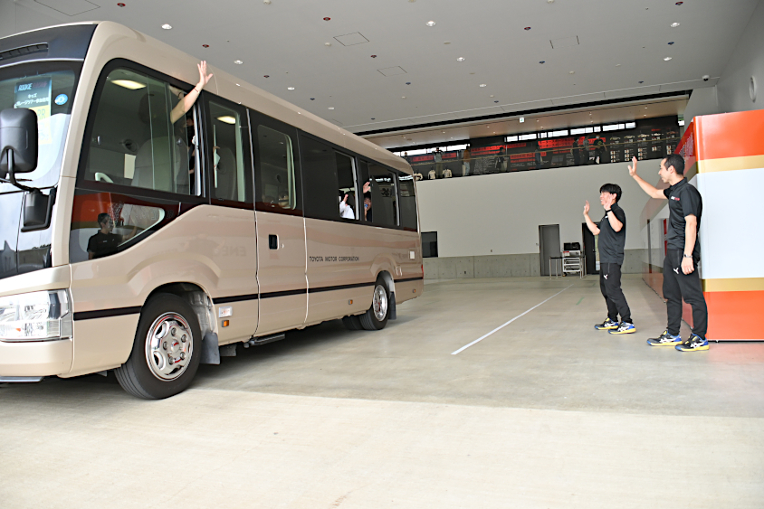 バスに乗ったROOKIE Racingキッズガレージツアーの参加者に手を振る寺尾チーフと錦織チーフ