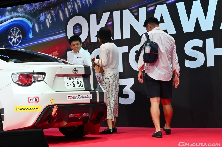 沖縄モーターショーで子連れの家族のお子さんをラリーチャレンジ用のGR86にご案内する高橋プレジデント