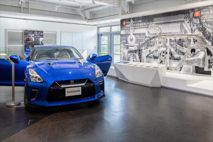 15馬力の7型エンジンの反対側に置かれたNISSAN GT-R。その出力は570馬力と強力な物だ。壁にはクルマができるまでの展示パネルが置かれている